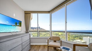 A modern hotel room with a large window offering a scenic view of a beach and mountains.