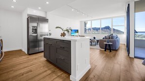 A modern kitchen with a large island, a built-in refrigerator, and a dining area with a view of mountains.