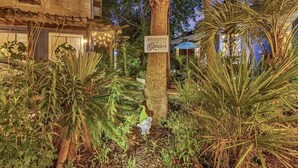 Un jardín bien cuidado con una palmera, un cartel que dice 'Bienvenido al Jardín' y un edificio con fachada rústica.