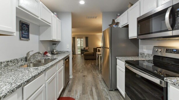 A modern kitchen with white cabinets, granite countertops, stainless steel appliances, and a wooden floor.