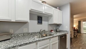 A kitchen with white cabinets, granite countertops, a stainless steel sink, and a dishwasher.