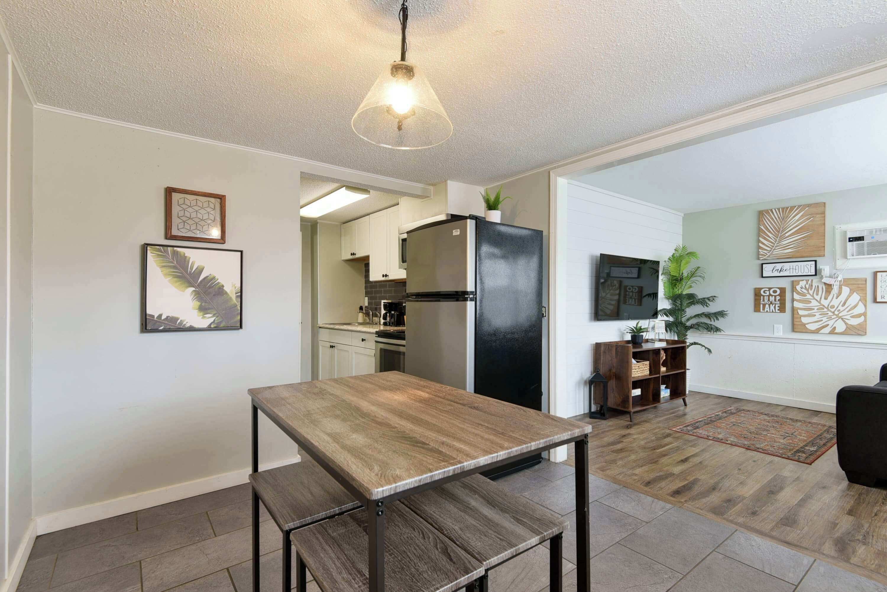 Una cocina moderna con refrigerador, mesa de comedor y banco. Hay cuadros en la pared y una planta en la esquina.