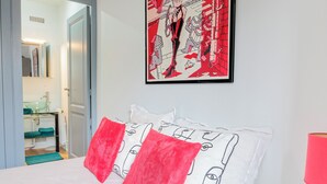 Una habitación de hotel con una cama, almohadas, una obra de arte enmarcada y un baño visible a través de una puerta abierta.