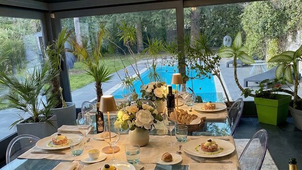 An outdoor dining area with a glass table, chairs, and a view of a swimming pool.