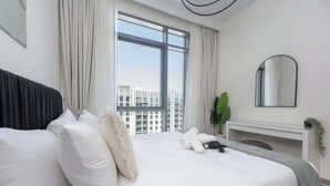 A modern hotel room with a large bed, a mirror, a fireplace, and a view of buildings.