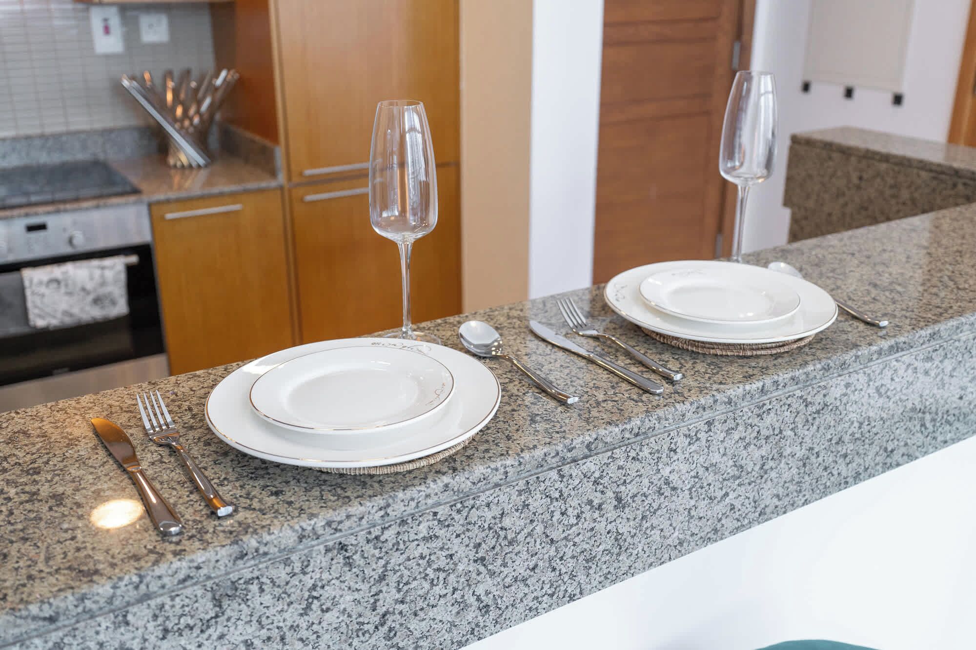 Un comptoir de cuisine avec une table mise pour deux personnes, comprenant des assiettes, des couverts et deux verres à vin.