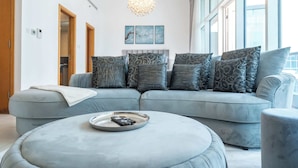 En moderne stue med en grå hjørnesofa, en rund fodskammel og en lysekrone.