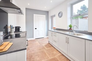 A modern kitchen with white cabinets, a black countertop, a stainless steel range hood, and a window with a view of the outside. - Host Stay The Beeches (Brampton)