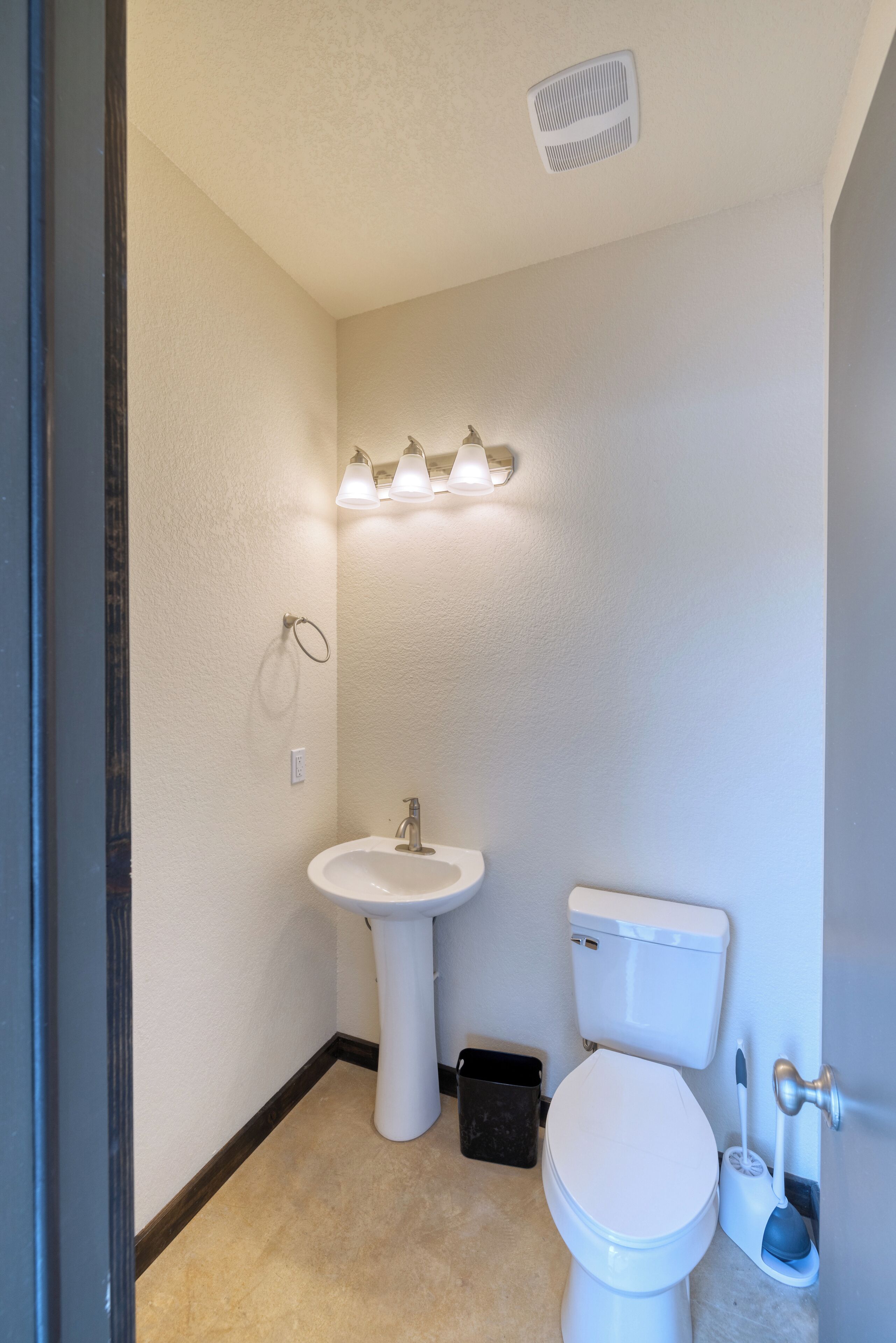 A bathroom with a pedestal sink, toilet, and a wall-mounted light fixture.