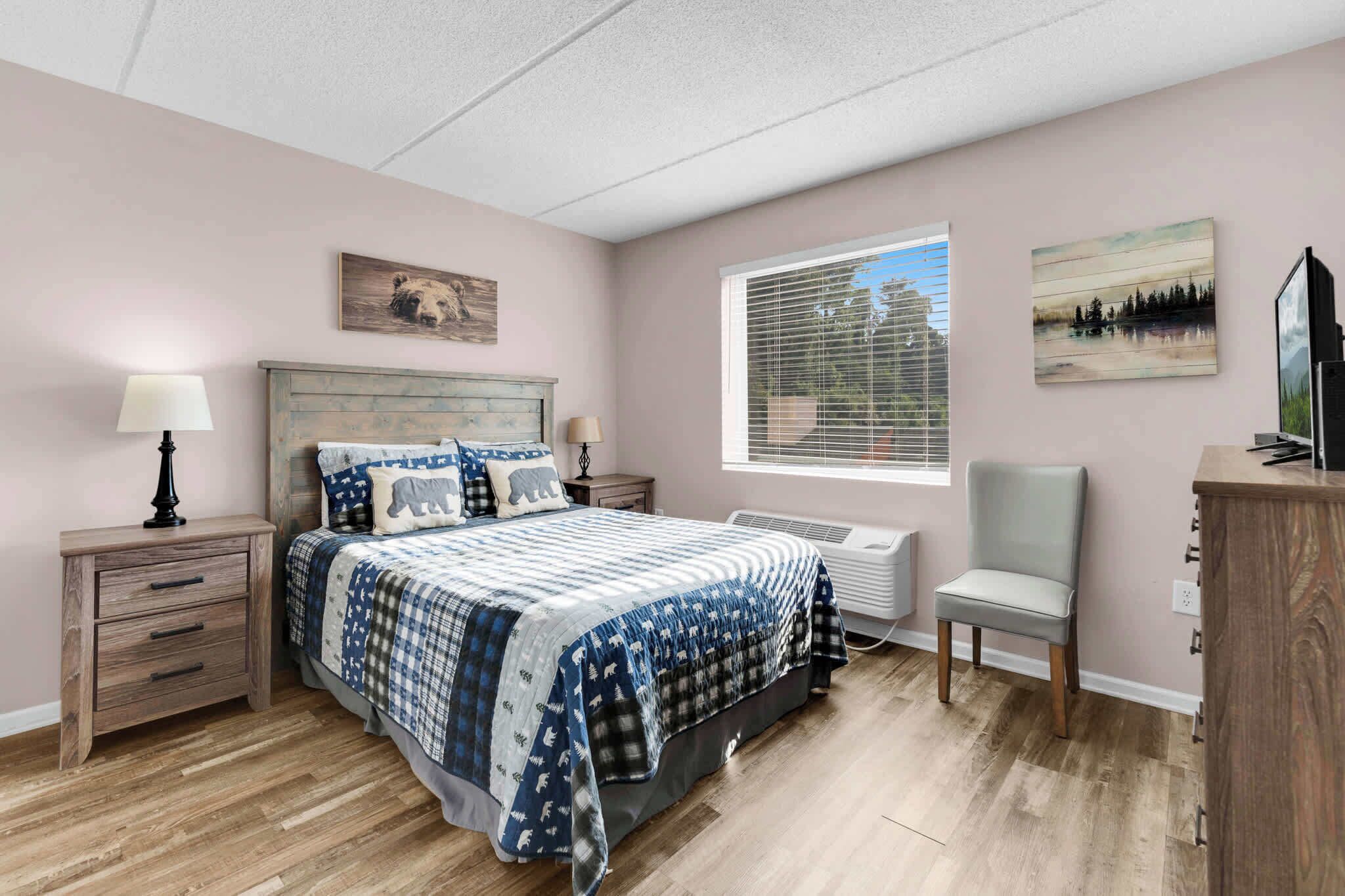 A bedroom with a bed, bedside tables, a chair, a dresser, a window with blinds, and wall art.