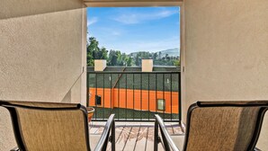 Ein Balkon mit zwei Stühlen und Blick auf ein Gebäude mit orange- und grün gefärbter Dachdeckung, vor blauem Himmel.