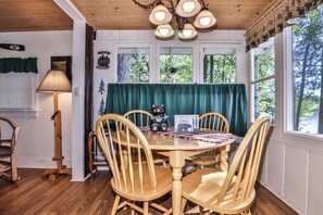 Interior acogedor de una cabaña con una mesa de comedor de madera rodeada de sillas, una lámpara y un letrero que dice "Moose Crossing".