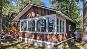 A wooden cabin with a large windowed porch, a picnic table, and a grill. - Stepaway Vacation Rentals-Cozy Cottage (St.Germain)