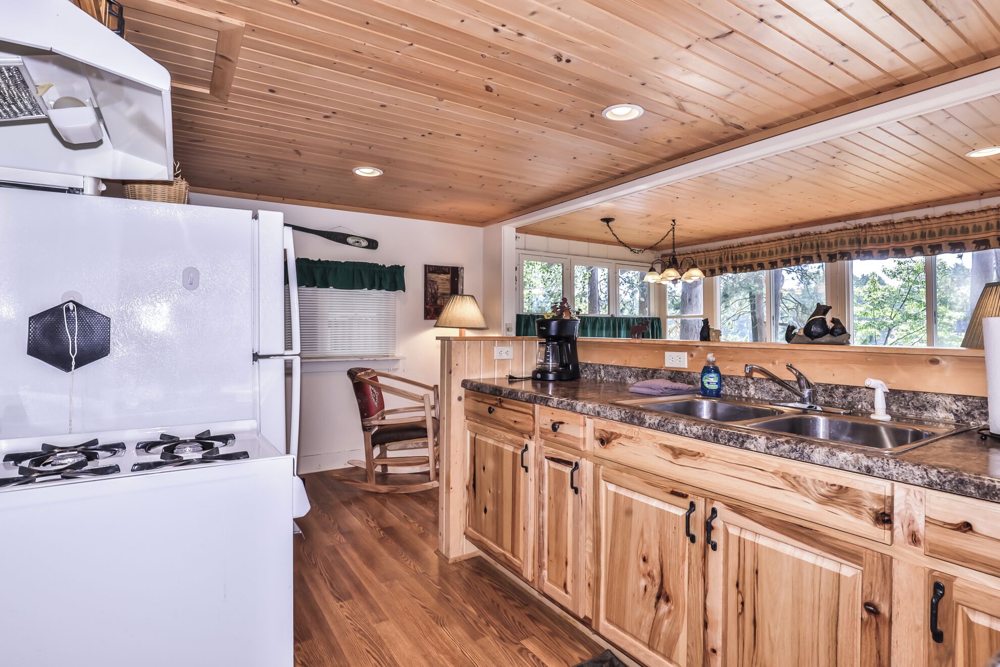 A kitchen with wooden cabinets, a granite countertop, a refrigerator, a stove, and a window with a view of trees.