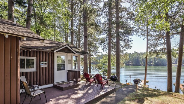 A cabin with a deck, outdoor seating, and a view of a lake. - Stepaway Vacation Rentals-Cozy Cottage (St.Germain)