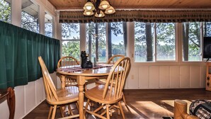 A dining area with a wooden table and chairs, a bear statue, and large windows overlooking a forested area. - Stepaway Vacation Rentals-Cozy Cottage (St.Germain)