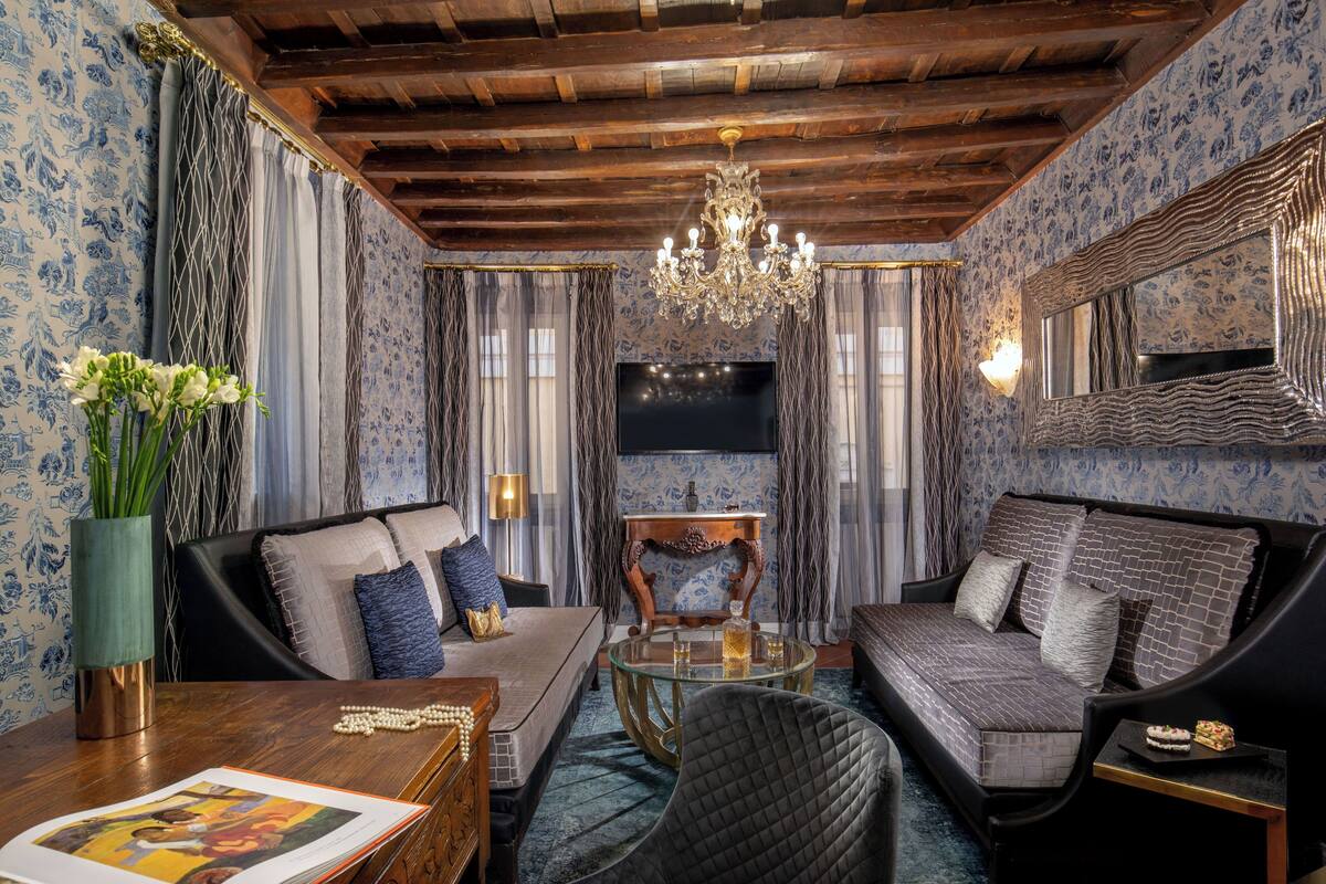 Una habitación con techo de madera, un candelabro, un sofá, una silla, una mesita de centro y un televisor.