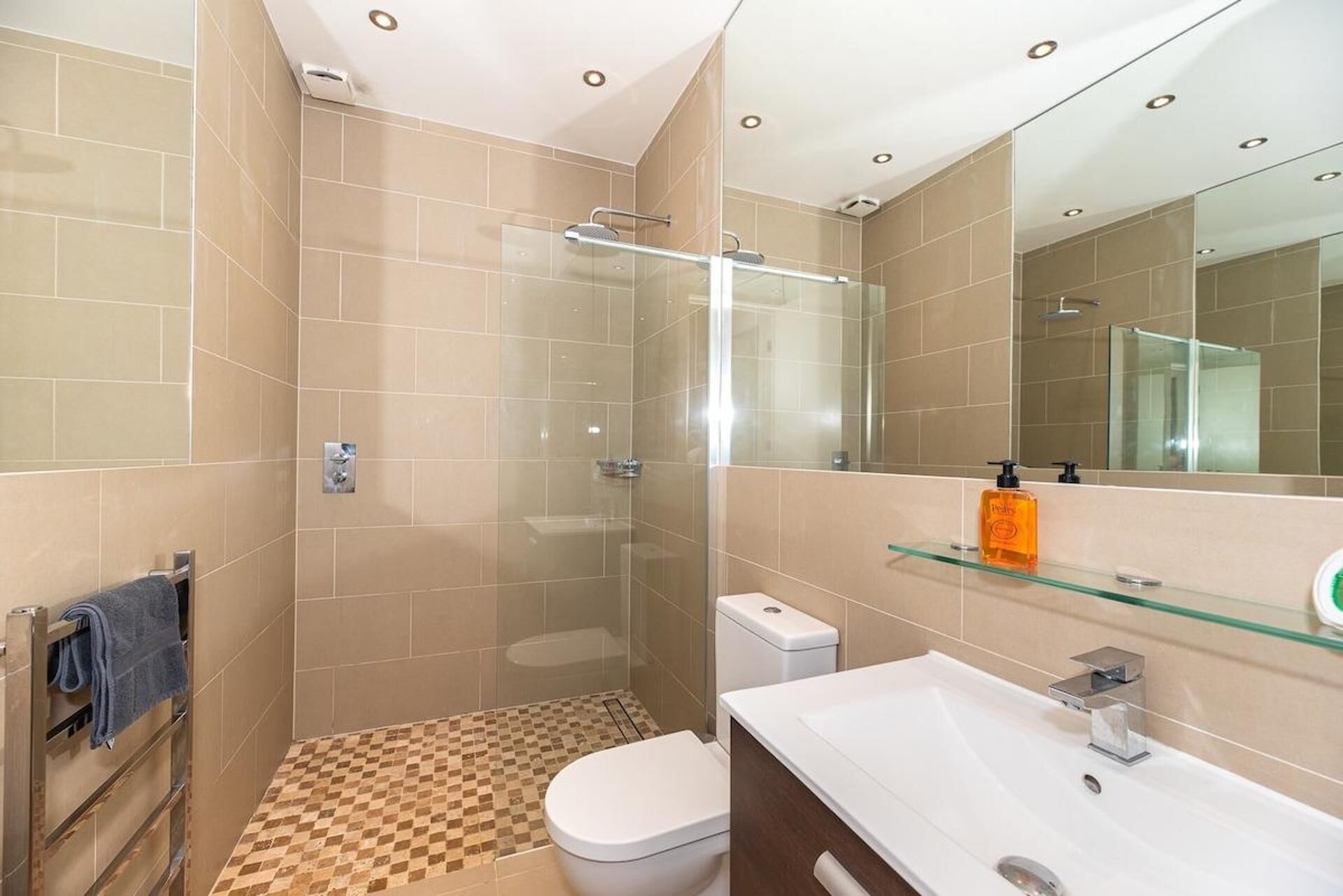 A modern bathroom with a glass shower enclosure, a white toilet, and a vanity with a glass shelf.