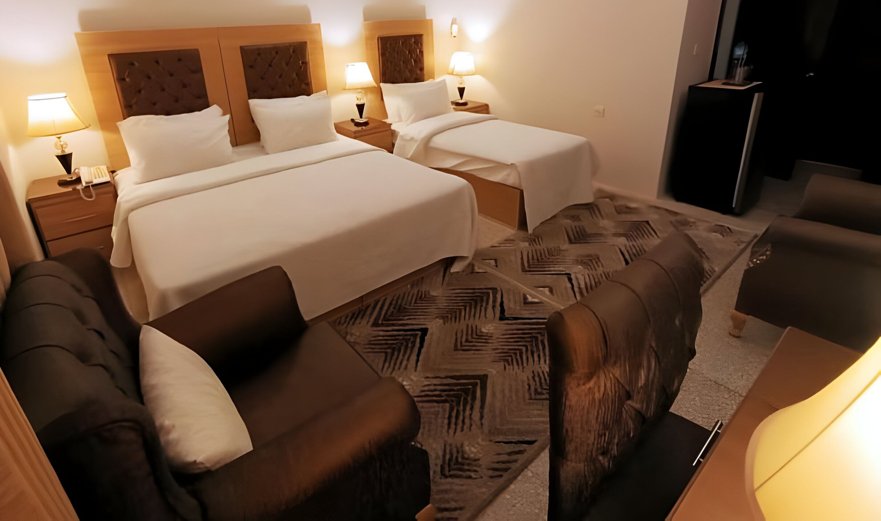 A hotel room with two beds, a sofa, a chair, and a small TV.