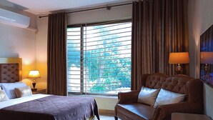 Habitación de hotel con cama, sofá de cuero, una mesita, lámpara y un ventanal con cortinas.