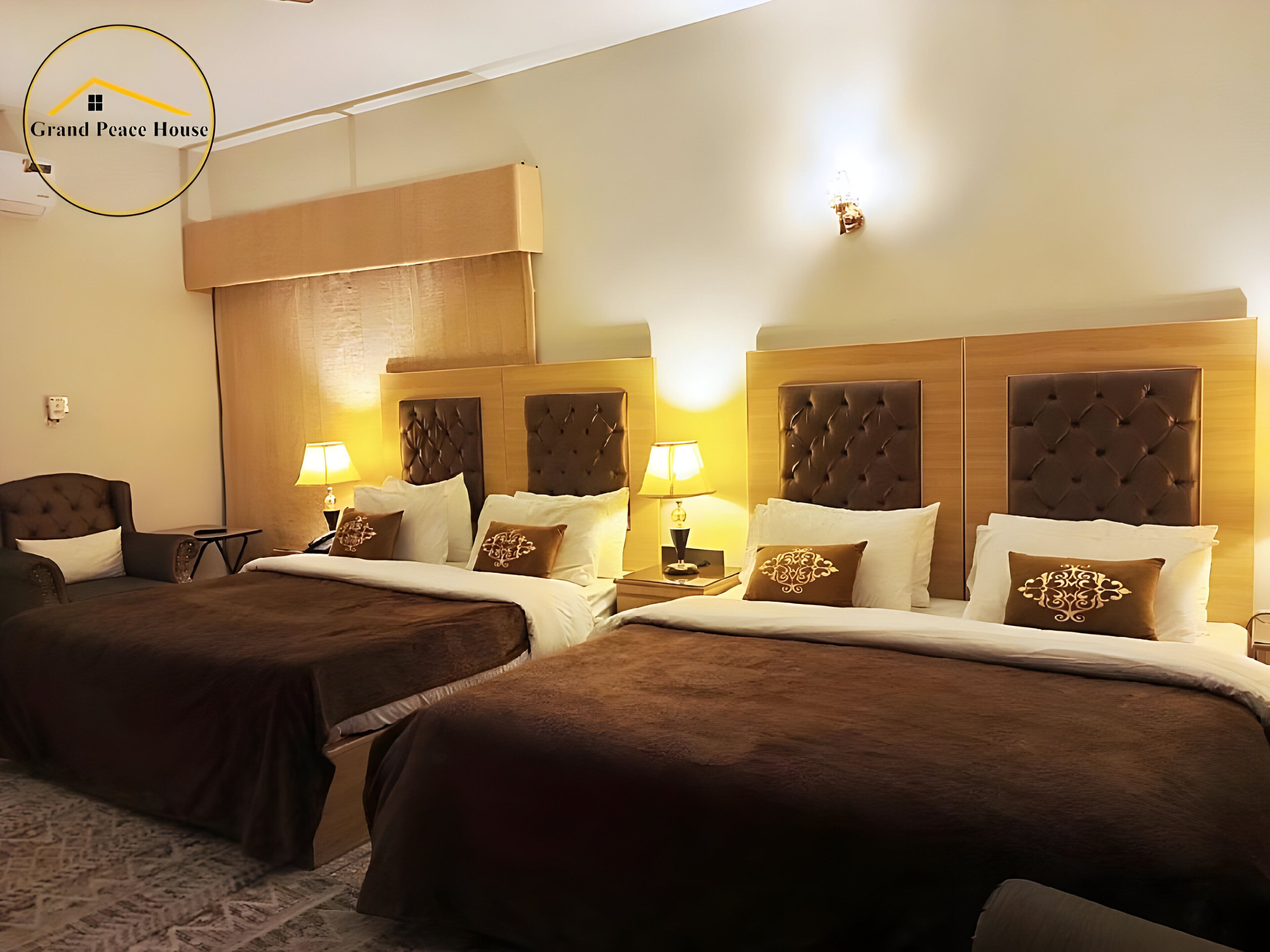 A hotel room with two beds, each with a brown headboard and white bedding. There are bedside tables with lamps, and the room has a neutral color scheme.