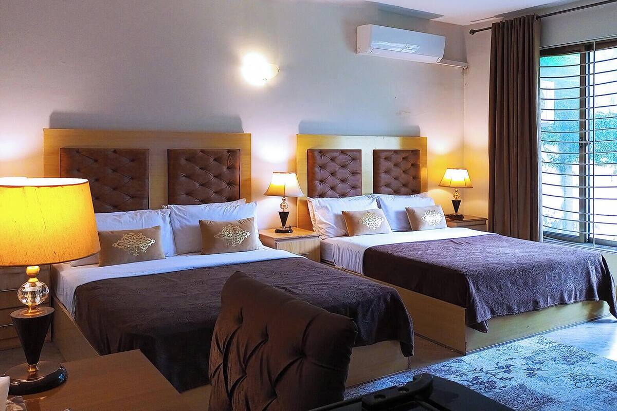 A hotel room with two beds, a sofa, a desk, and a window with blinds.