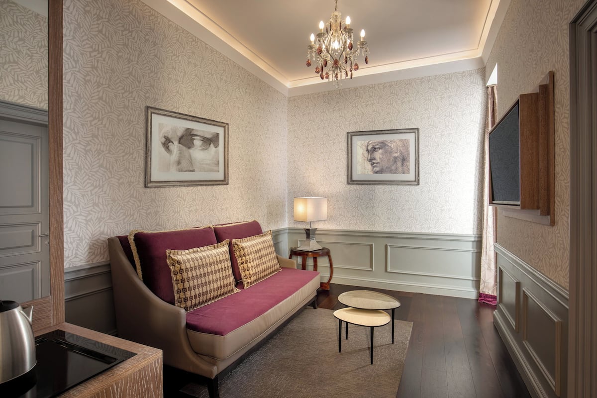 A room with a sofa, two side tables, a chandelier, and framed artwork on the walls.