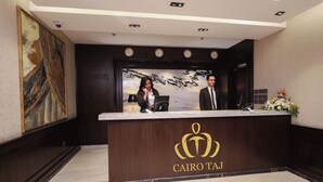 A reception desk with a logo, a large painting, and clocks on the wall.