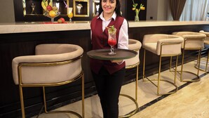 A bar area with a bartender holding a drink, bar stools, and a marble countertop.