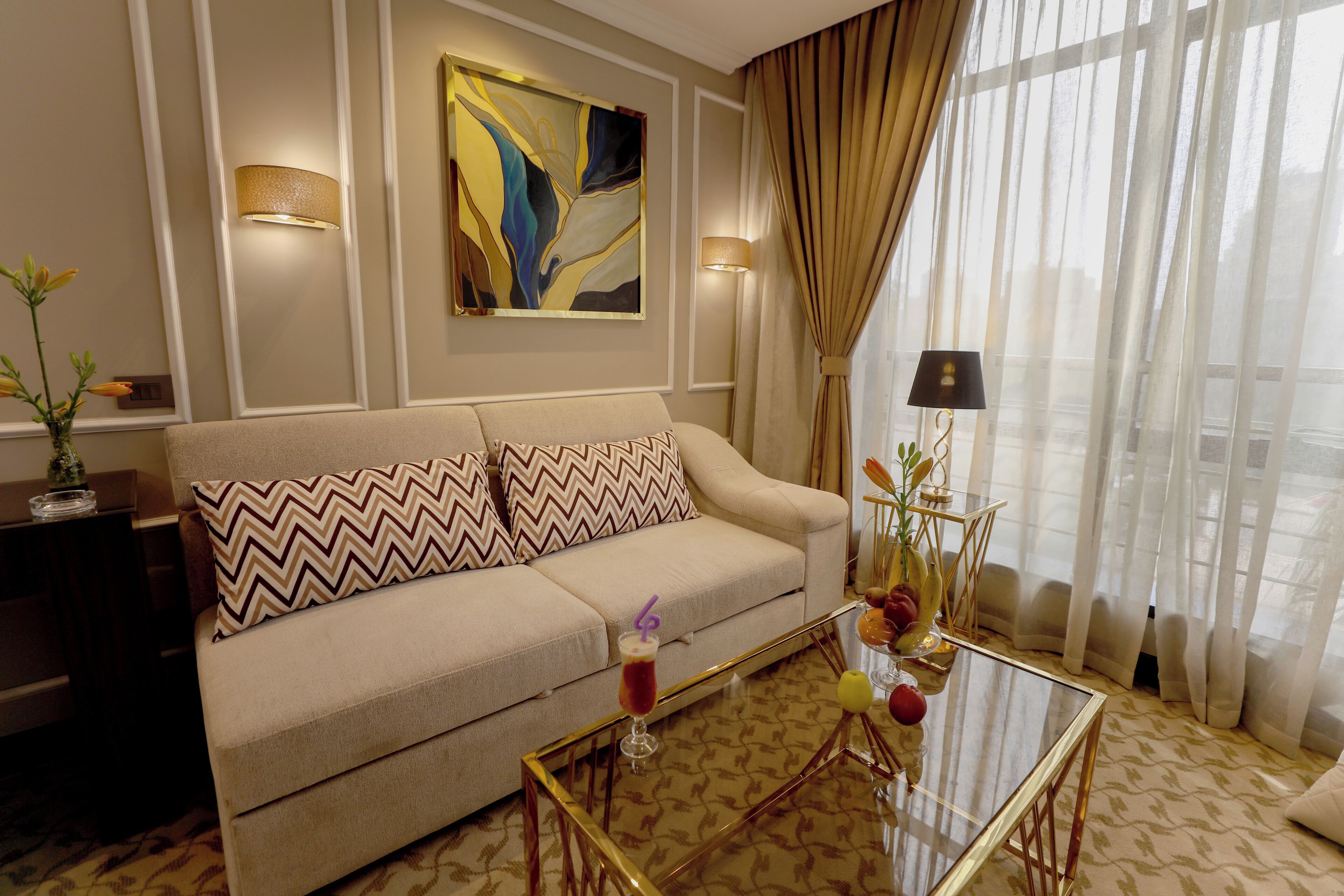 Una sala de estar con un sofá color beige, cojines estampados, una mesa de centro de vidrio y un cuadro en la pared.