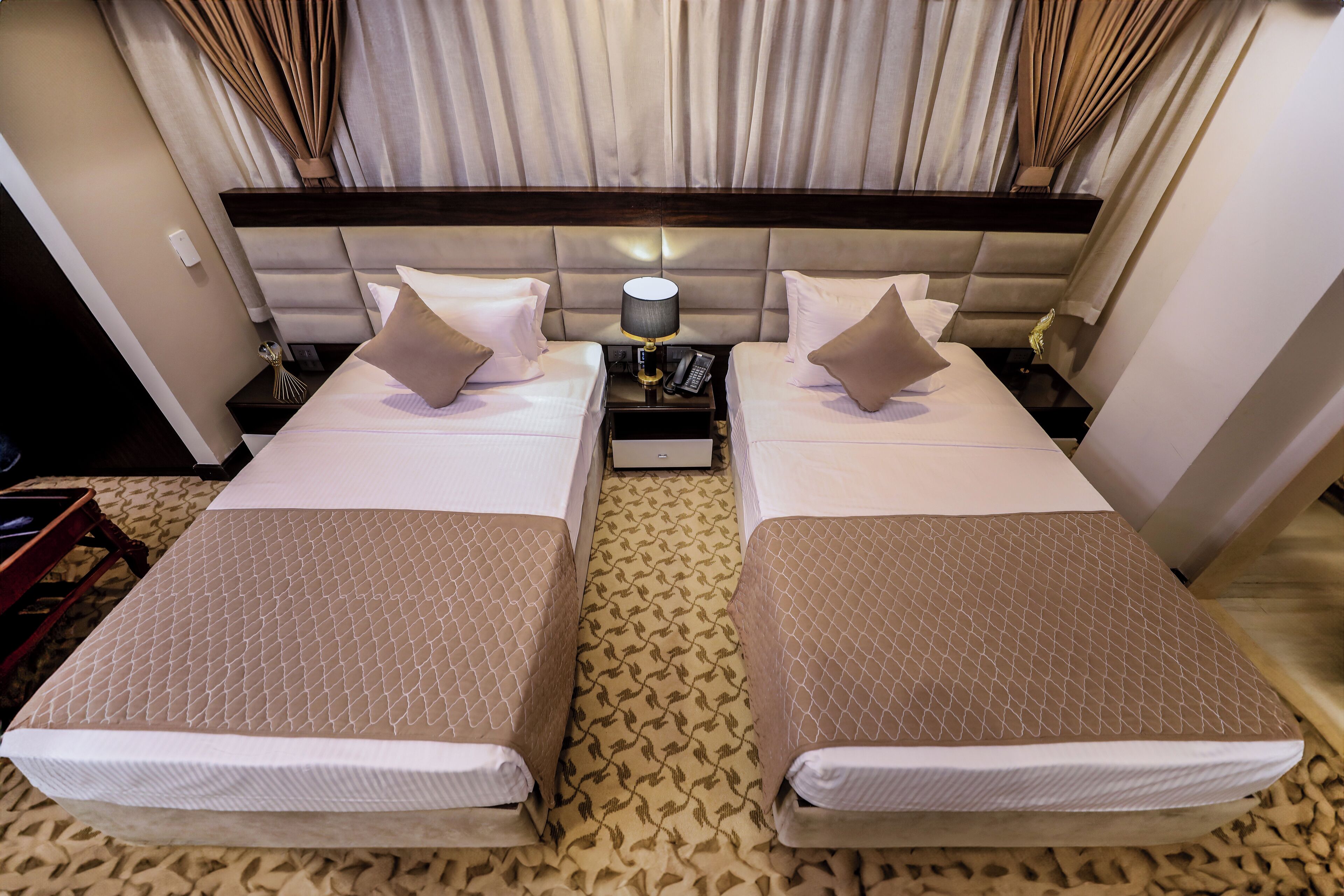 A hotel room with two beds, a nightstand with a lamp, and a patterned carpet.