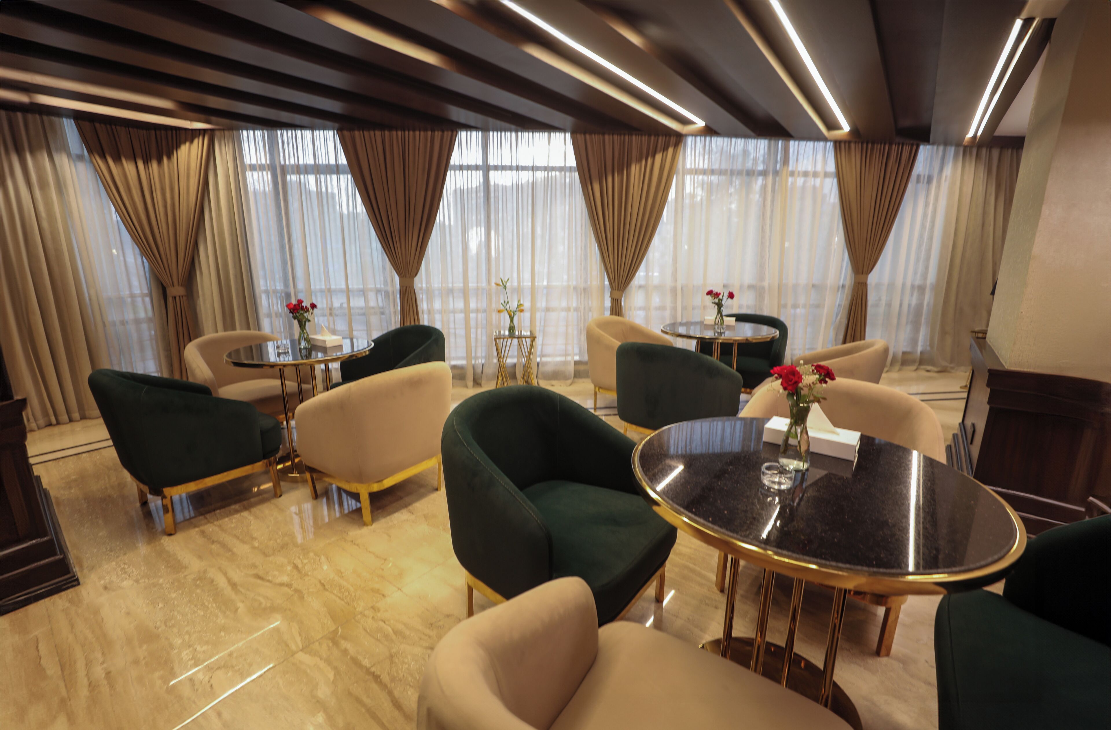 Un moderno vestíbulo de hotel con sillones verde y beige, una mesa redonda y un jarrón con flores.