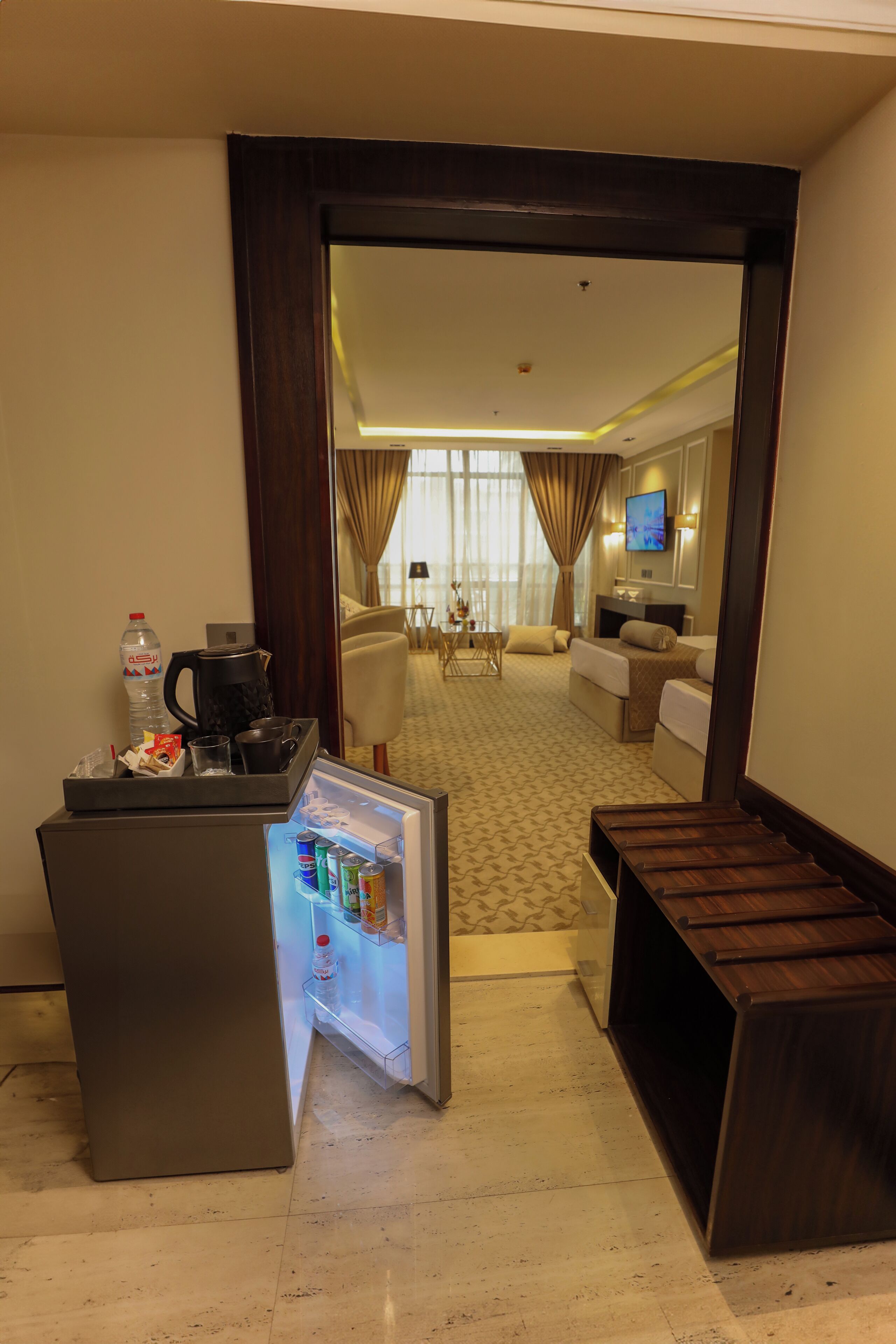 Une chambre d’hôtel équipée d’un minibar, d’un coin salon avec un canapé et des fauteuils, d’une télévision et donnant sur la chambre voisine.