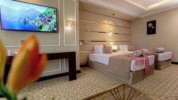 A hotel room with a large flat-screen TV, a bed with two pillows, a bedside table, and a wall-mounted lamp.