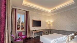 Une chambre d’hôtel comprenant un lit, un bureau, deux chaises, une télévision et une fenêtre donnant sur un immeuble.