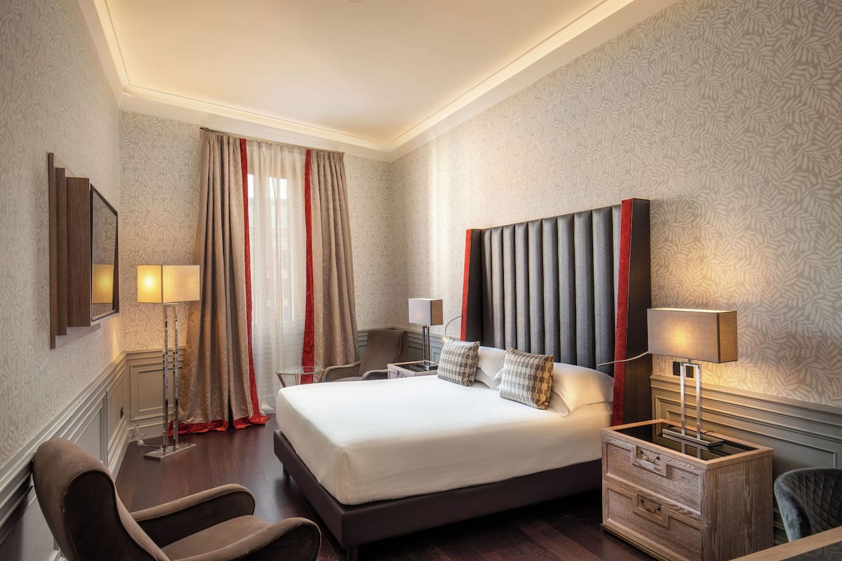 A hotel room with a large bed, two bedside tables with lamps, a chair, and a nightstand with drawers.
