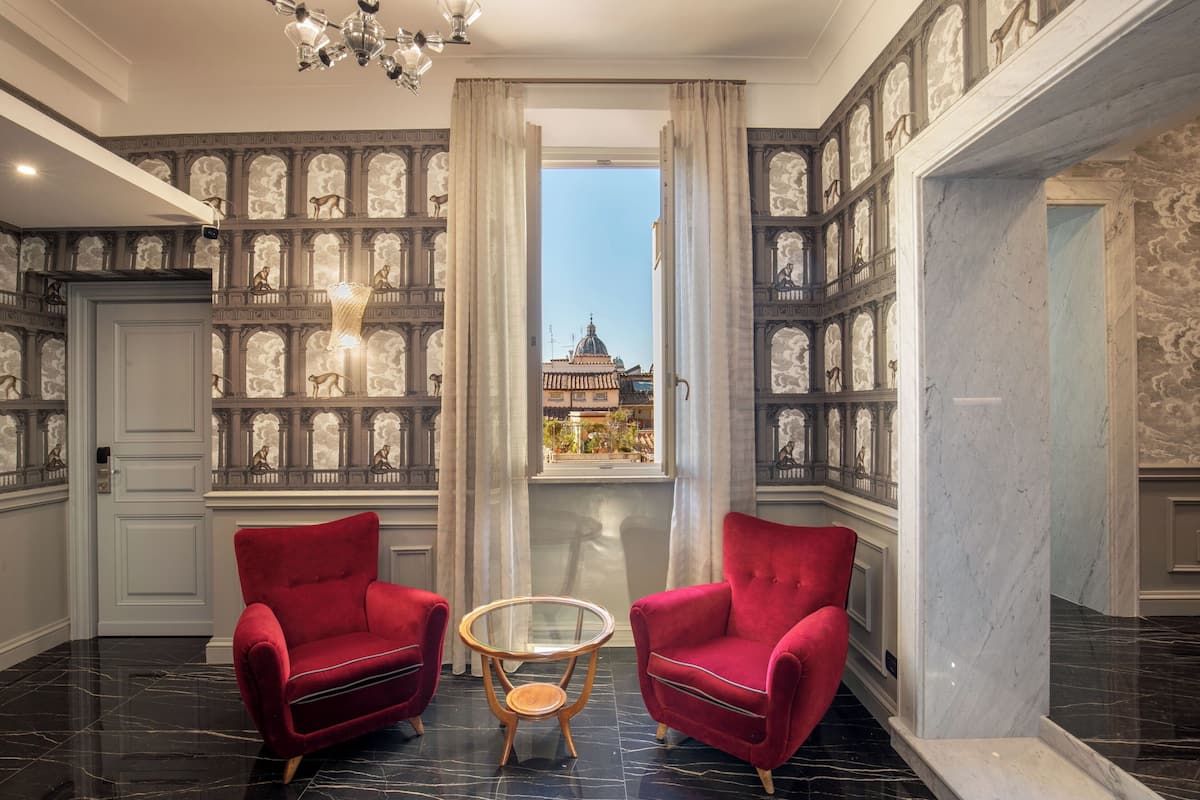 A room with two red armchairs, a glass table, and a view of a building through a window with curtains.