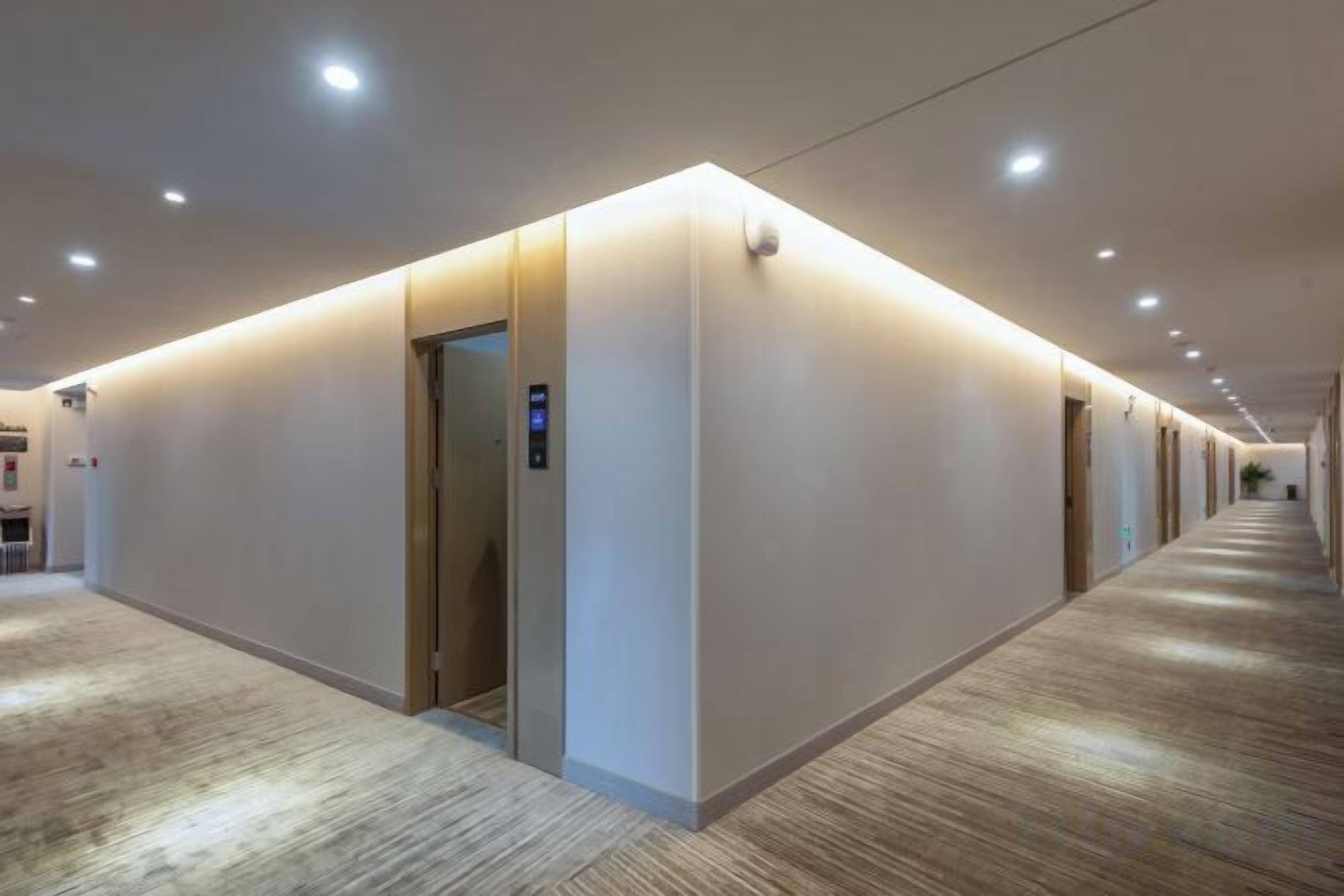 A hotel corridor with a carpeted floor, a wall-mounted elevator, and recessed lighting.