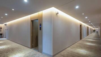 A hotel corridor with a carpeted floor, a wall-mounted elevator, and recessed lighting.