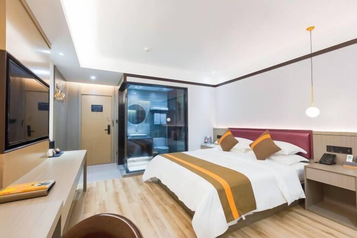 A modern hotel room with a large bed, a desk, a mirror, and a wardrobe.