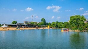 A lake with a boat, buildings, and trees in the background. - GYA Hotel (Jiaxing Nanhu Scenic Area Nanhu Tiandi) (Jiaxing)