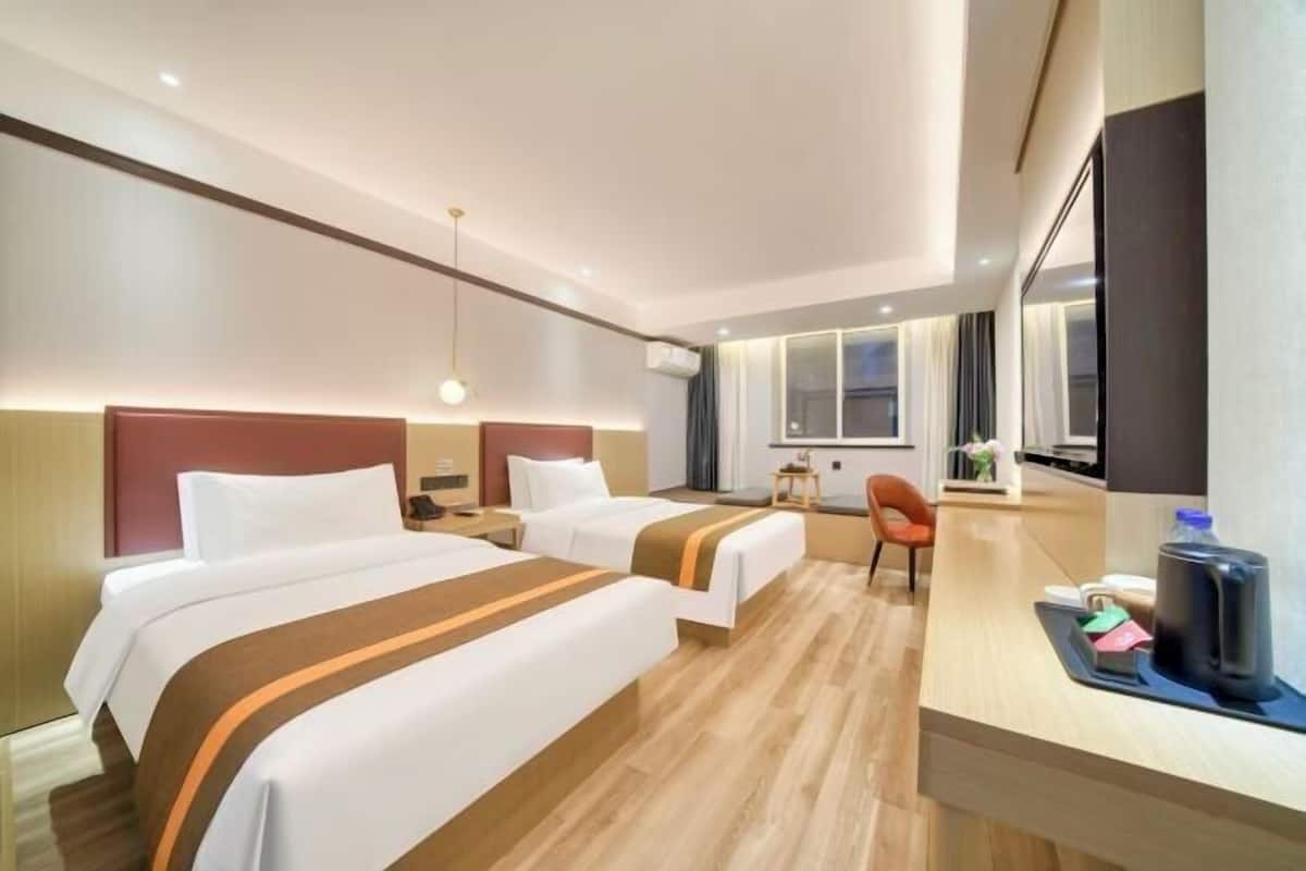 A hotel room with two beds, a desk, a chair, and a large window.