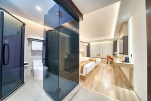 A modern hotel room with a glass shower enclosure, a separate toilet, a bed with a headboard, a desk, and a chair.