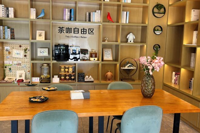 A room with a wooden table, chairs, a bookshelf, and a decorative vase with flowers.