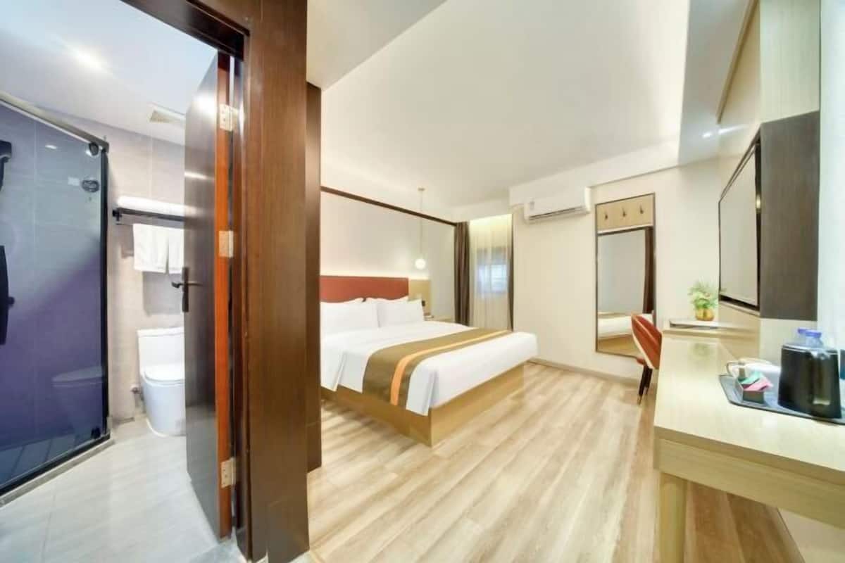 A hotel room with a bed, a desk, a mirror, a shower, and a toilet.