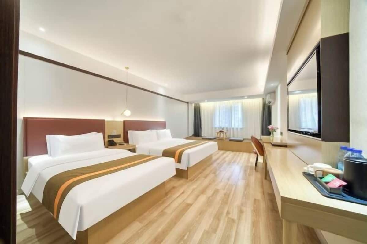 A hotel room with two beds, a desk, a chair, a TV, and a window with curtains.