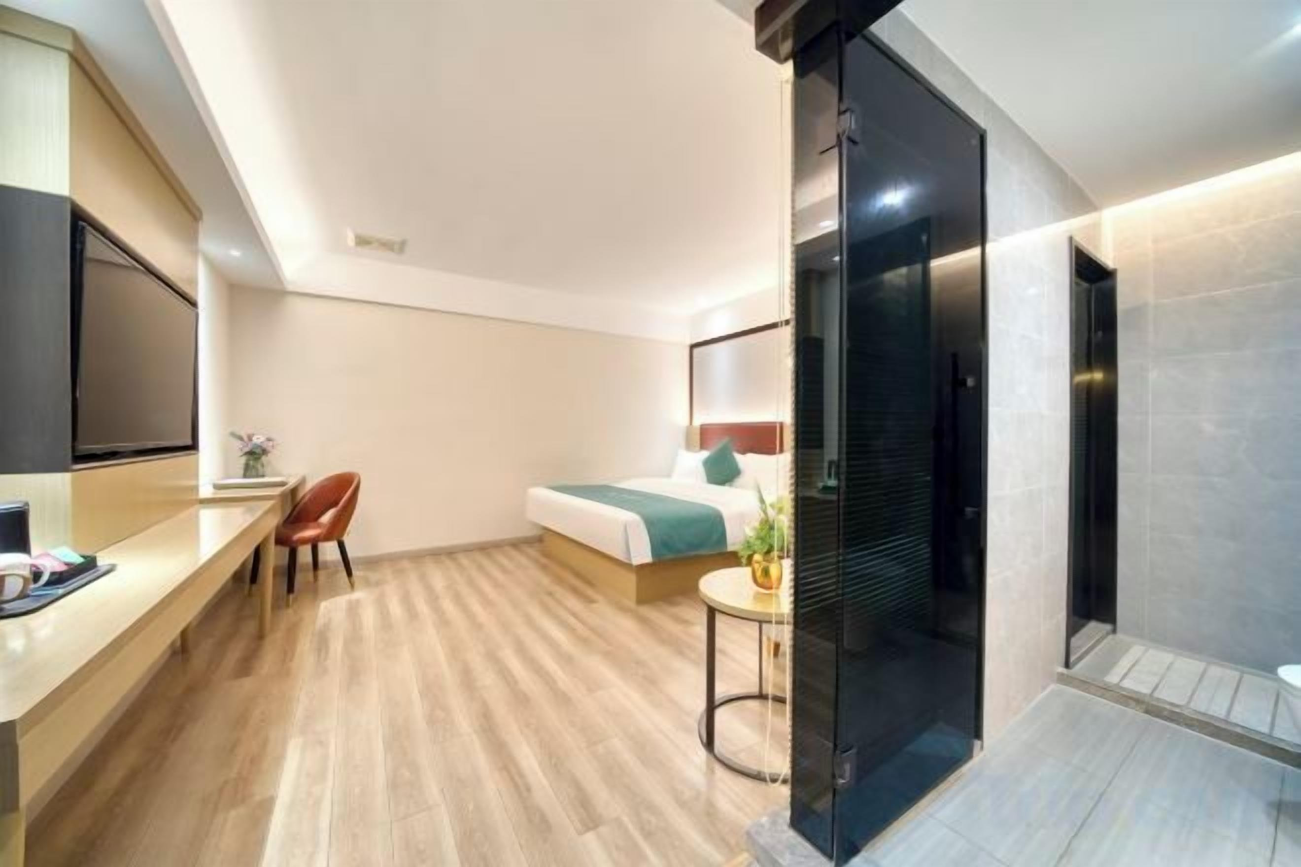 A modern hotel room with a bed, desk, chair, and a small table with a plant.