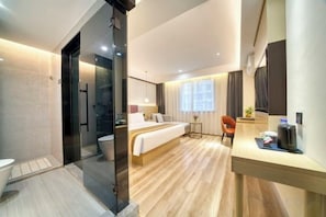 Una habitación de hotel moderna con suelo de madera, una cama, un escritorio y un baño con cabina de ducha de vidrio.