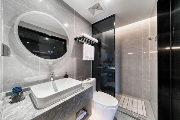 A modern bathroom with a large oval mirror, a white sink, a toilet, and a glass shower enclosure. - GYA Hotel (Jiaxing Nanhu Scenic Area Nanhu Tiandi) (Jiaxing)