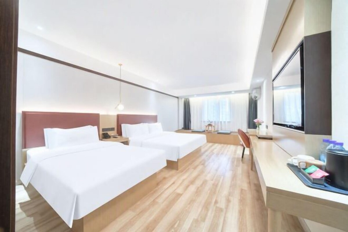 Hotellihuone, jossa on kaksi sänkyä, työpöytä ja suuri ikkuna.